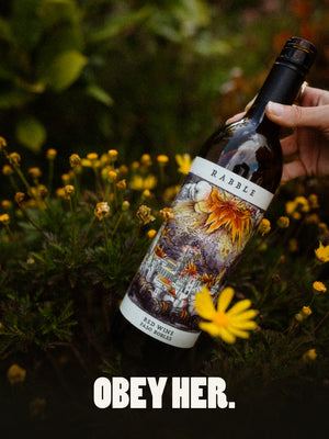Red Wine bottle in a flower field with the caption "Obey Her"